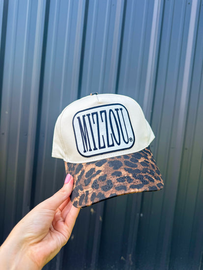 Cap with 'Mizzou' logo and leopard print brim held against a metallic wall.